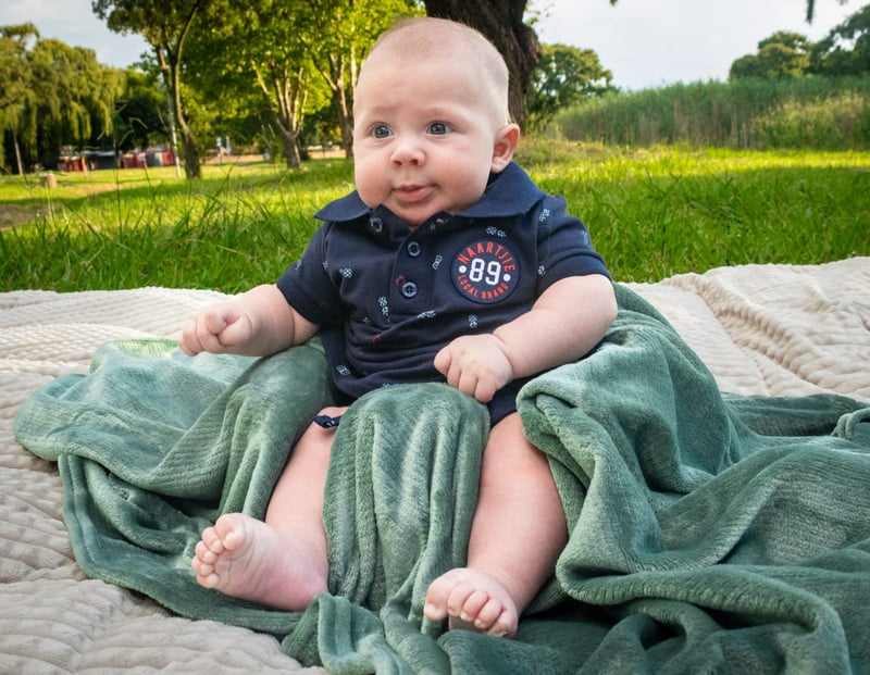 a baby sitting on a blanket in the grass