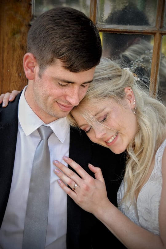 A bride and groom smiling at each other in front of a window