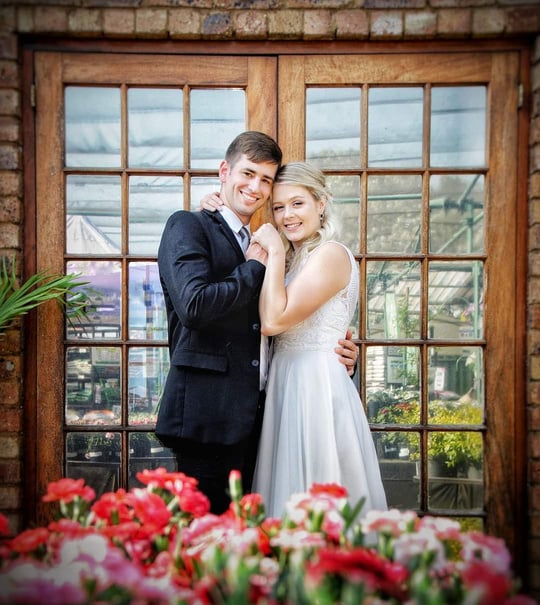 A bride and groom pose for a photo in front of a flower shop